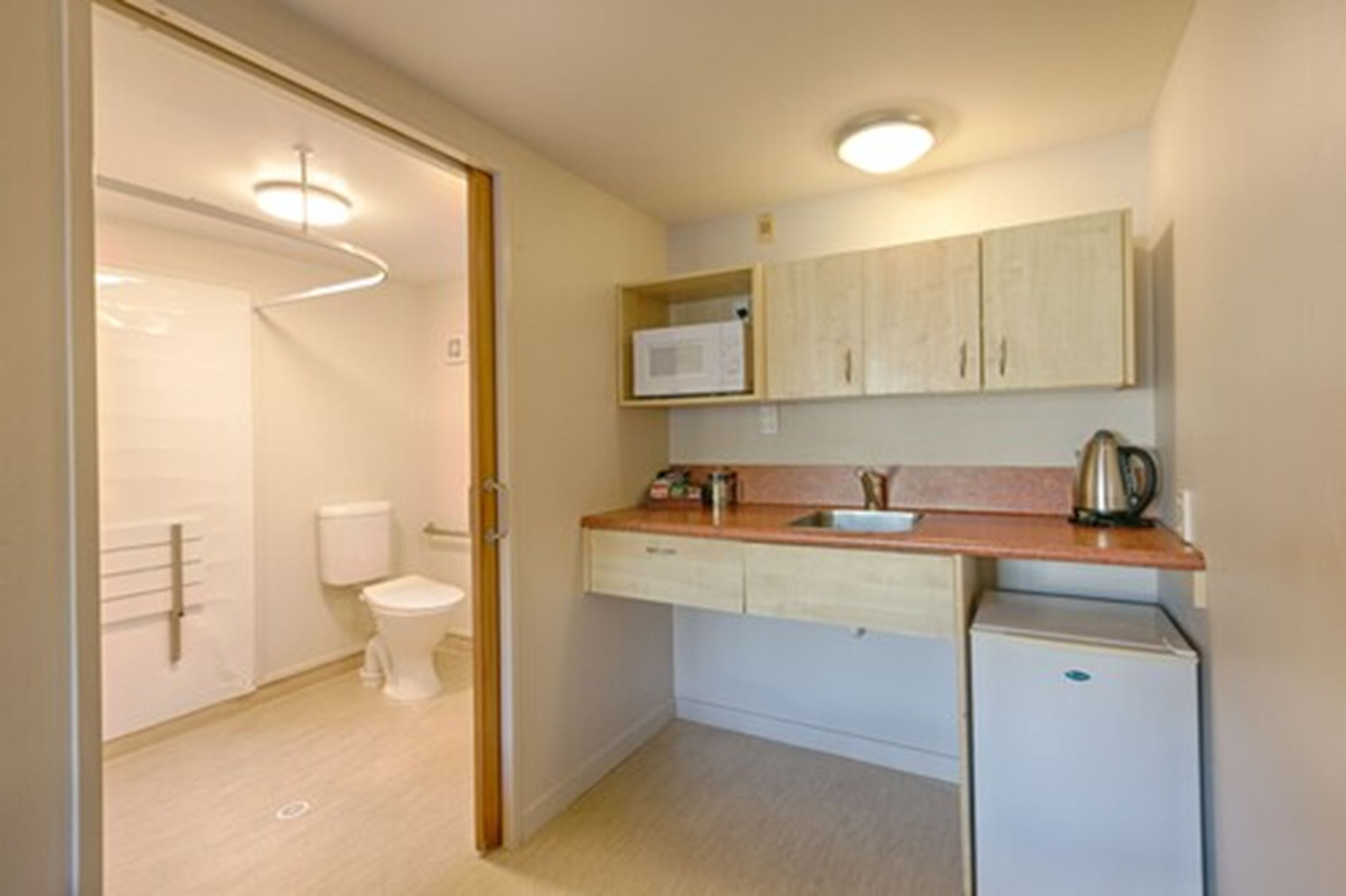 A compact kitchen with a microwave, kettle, and a small refrigerator.