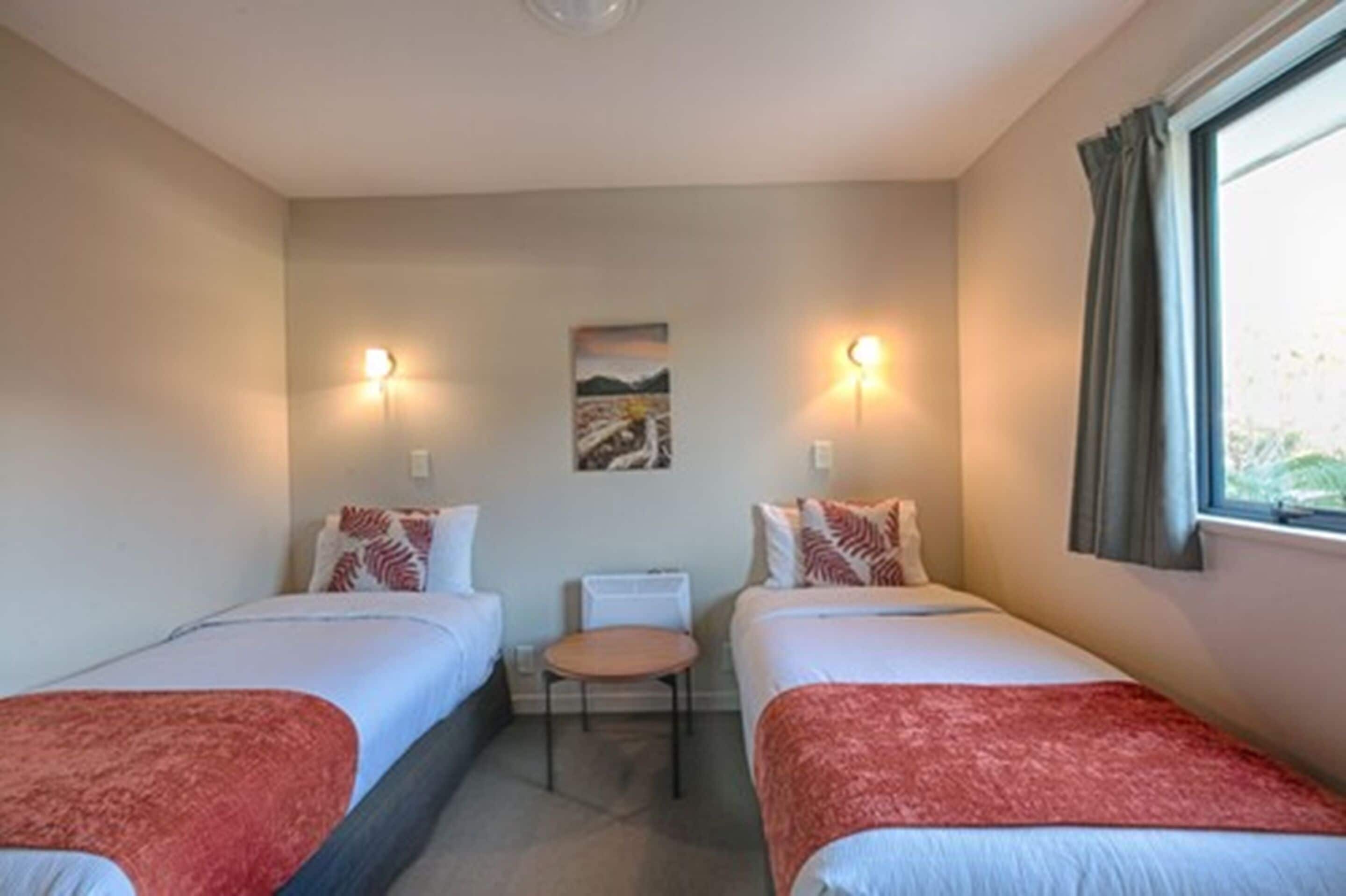 A hotel room with two beds, a small table, and a window with curtains.