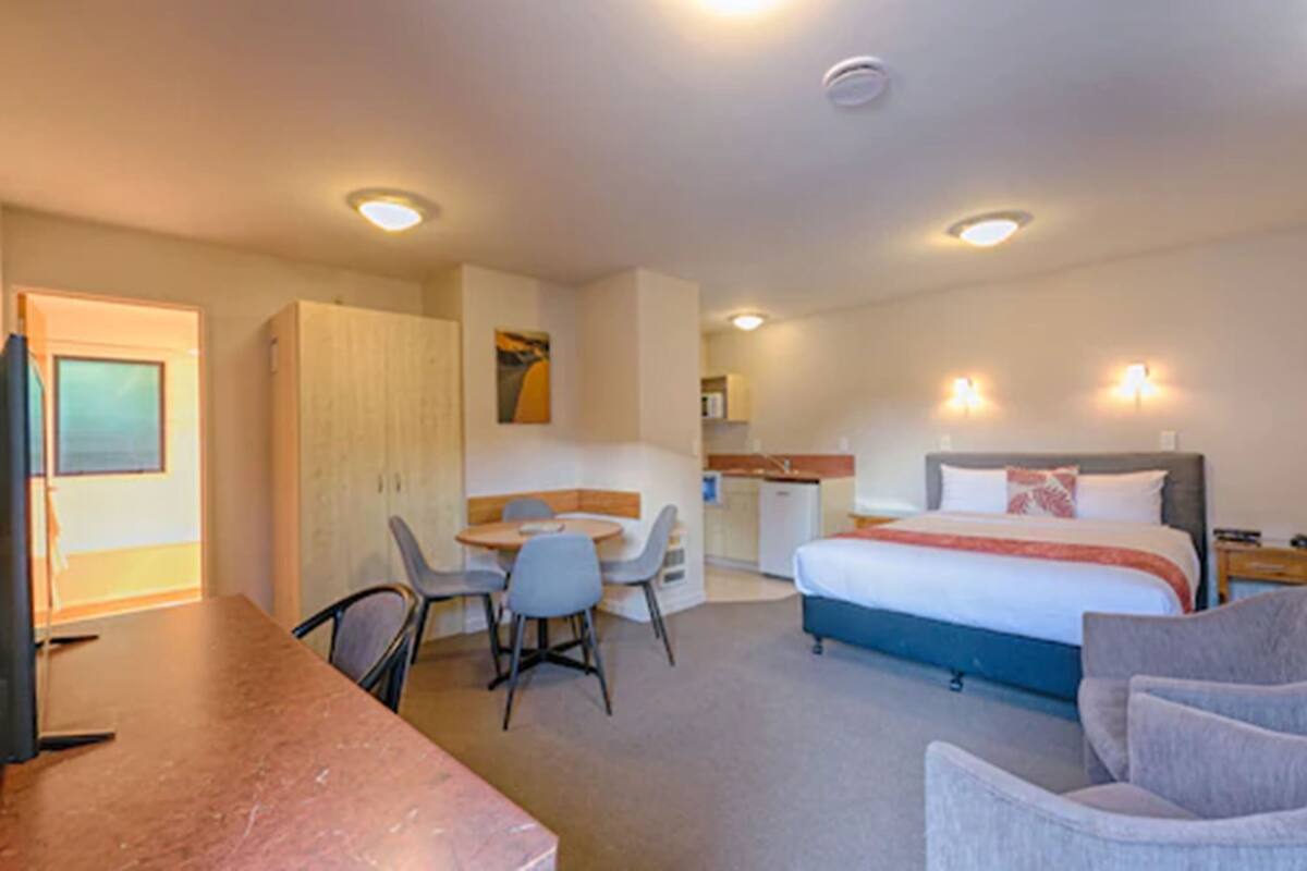 A hotel room with a bed, a desk, a chair, a small kitchenette, and a wardrobe.