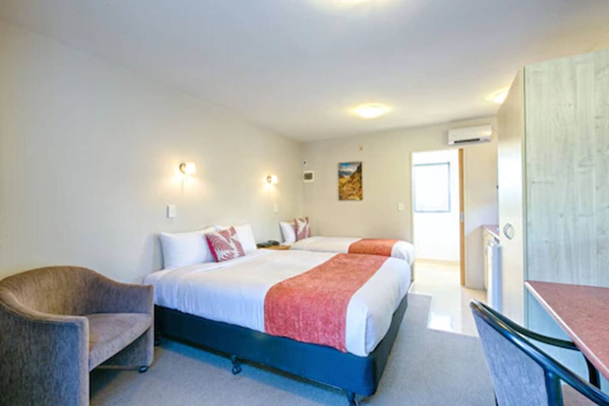 A hotel room with two beds, a chair, a desk, and a door leading to the bathroom.