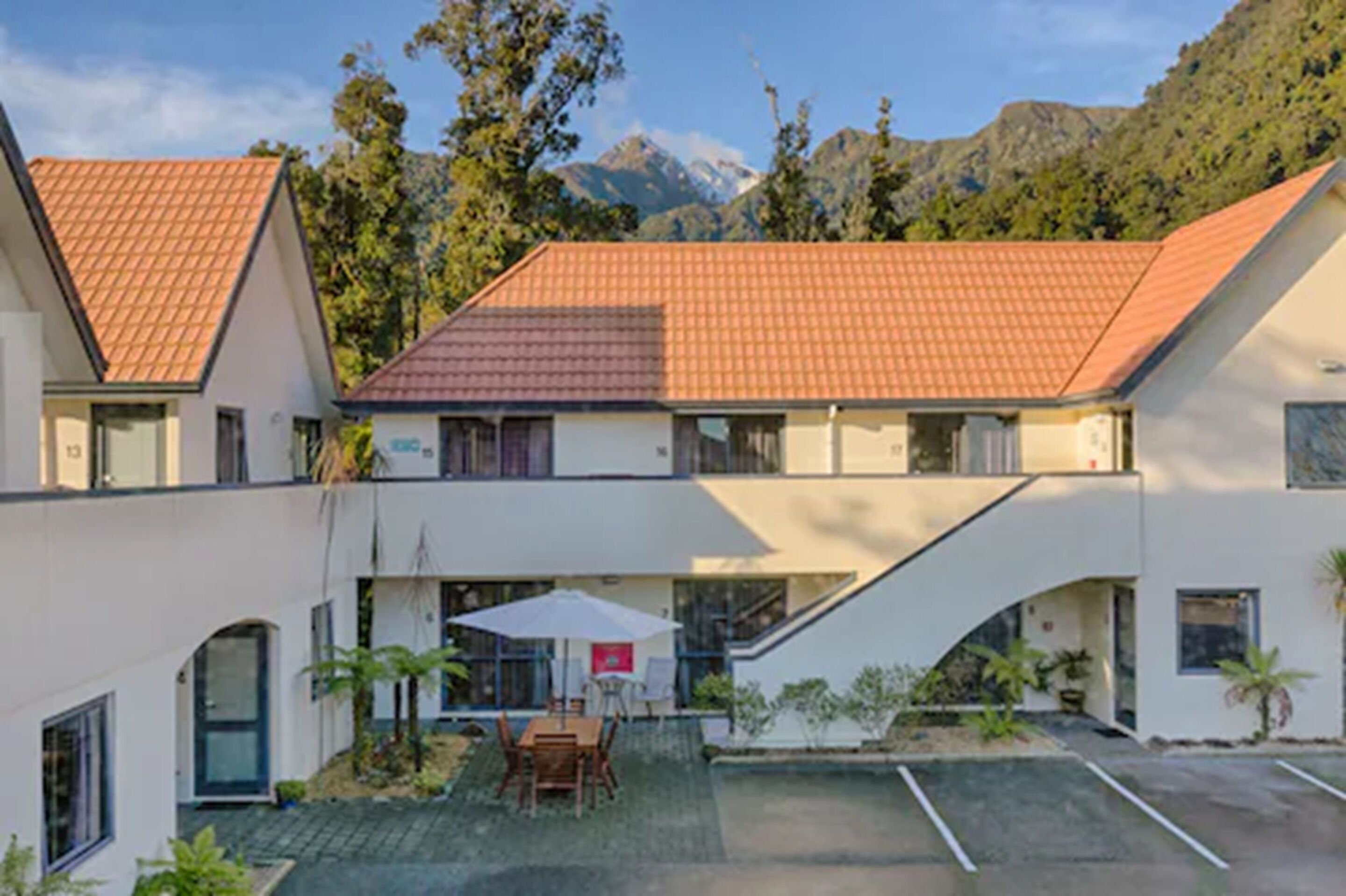 A two-story building with a red-tiled roof, a covered patio with outdoor furniture, and a mountain backdrop.