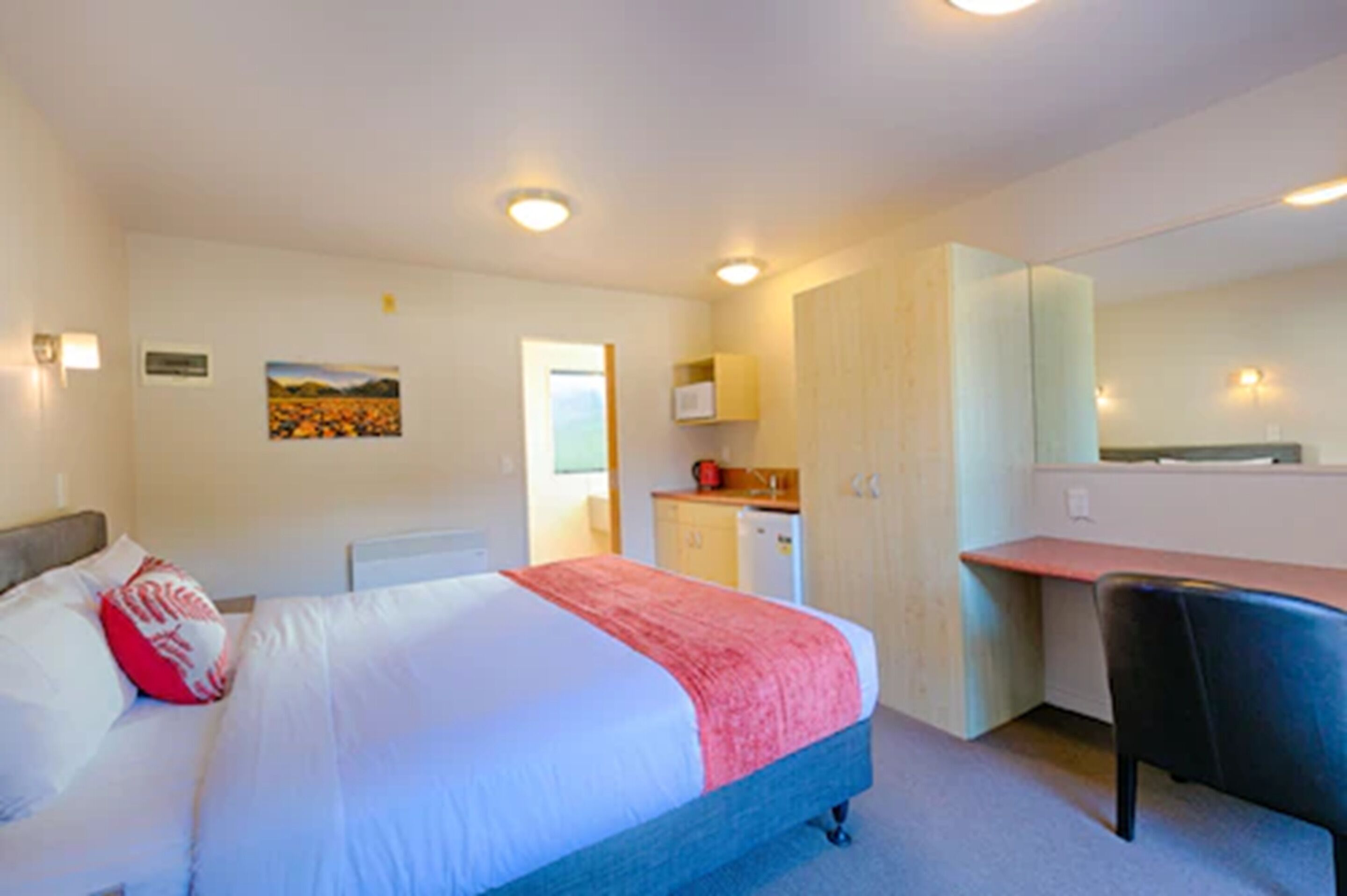 Une chambre d’hôtel comprenant un lit, un bureau, une chaise, une petite kitchenette et une salle de bain.