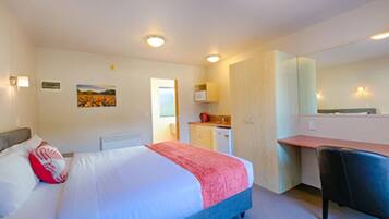 Une chambre d’hôtel comprenant un lit, un bureau, une chaise, une petite kitchenette et une salle de bain.