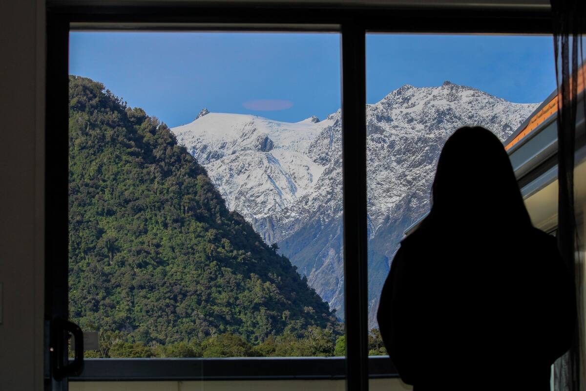 A view of a mountainous landscape through a window, with a silhouette of a person in the foreground.