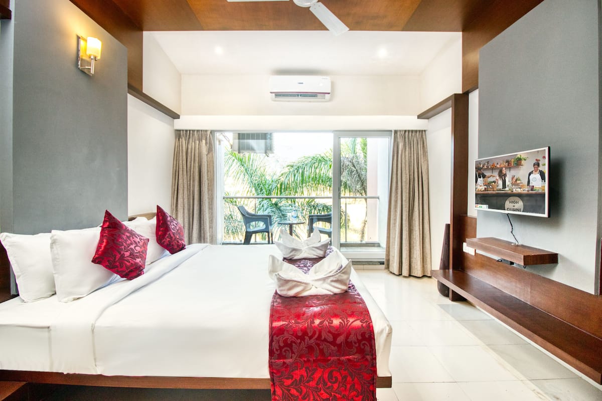 A hotel room with a bed, a TV, a balcony with a table and chairs, and an air conditioning unit.