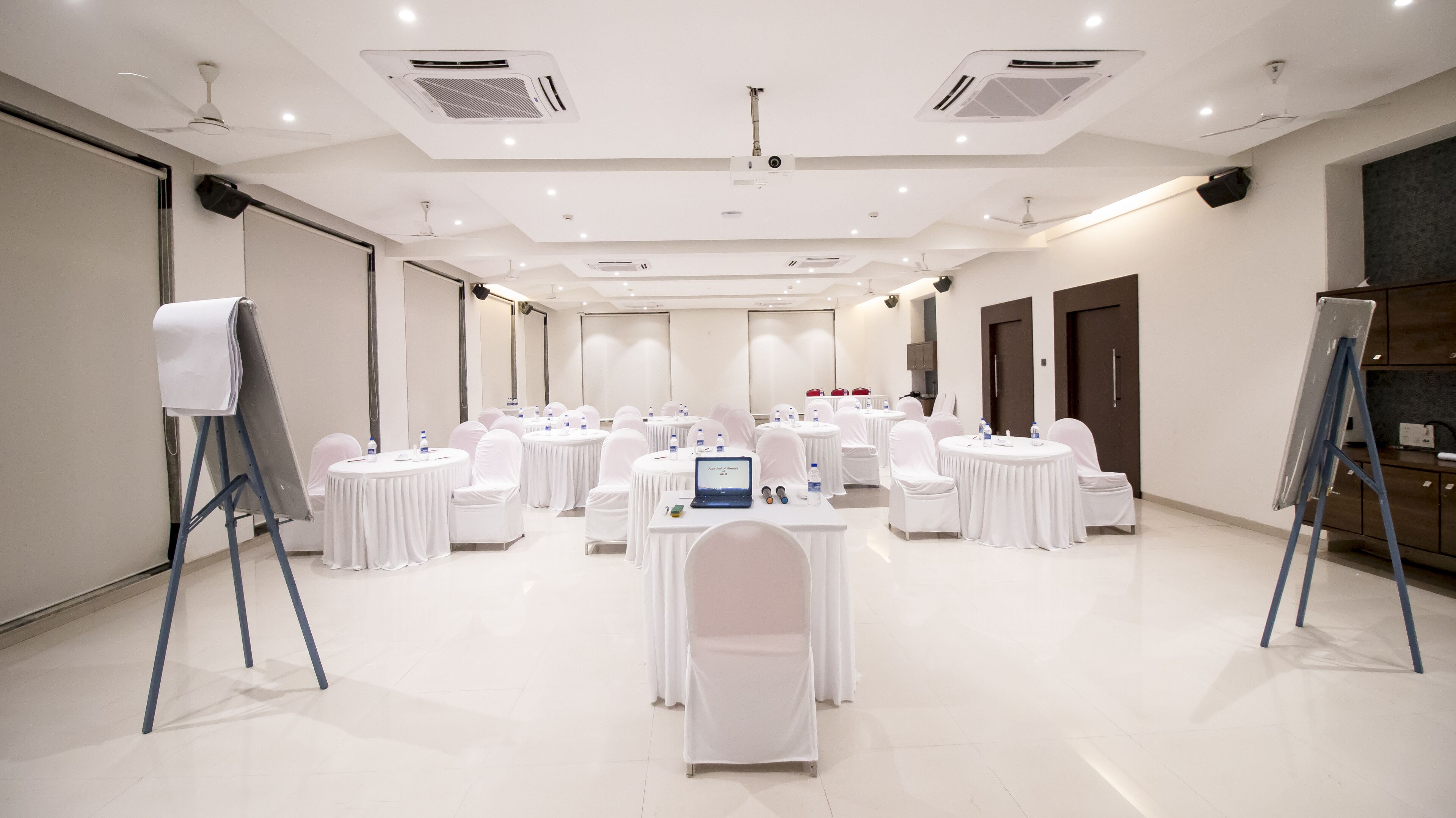 A conference room with multiple round tables, white chairs, and a whiteboard.