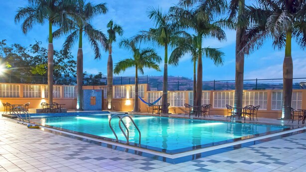 A pool area with palm trees, lounge chairs, and a view of distant hills. - 7 Apple Resort Lonavala (Mawal)