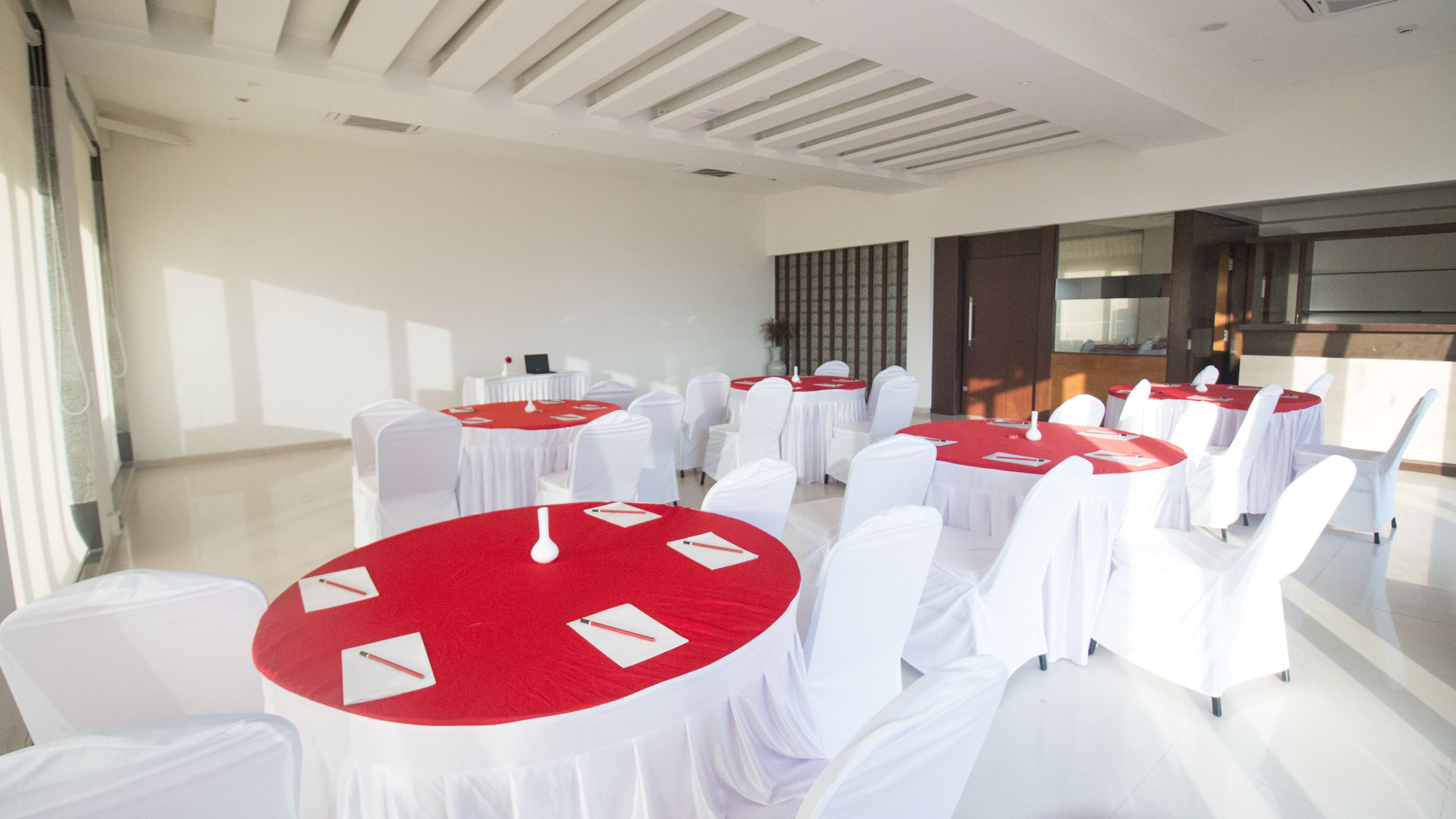 Une salle de conférence avec des tables rondes recouvertes de nappes rouges, des chaises blanches et un design de plafond moderne.