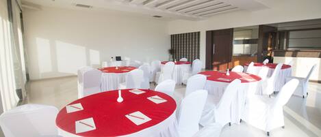 Une salle de conférence avec des tables rondes recouvertes de nappes rouges, des chaises blanches et un design de plafond moderne.