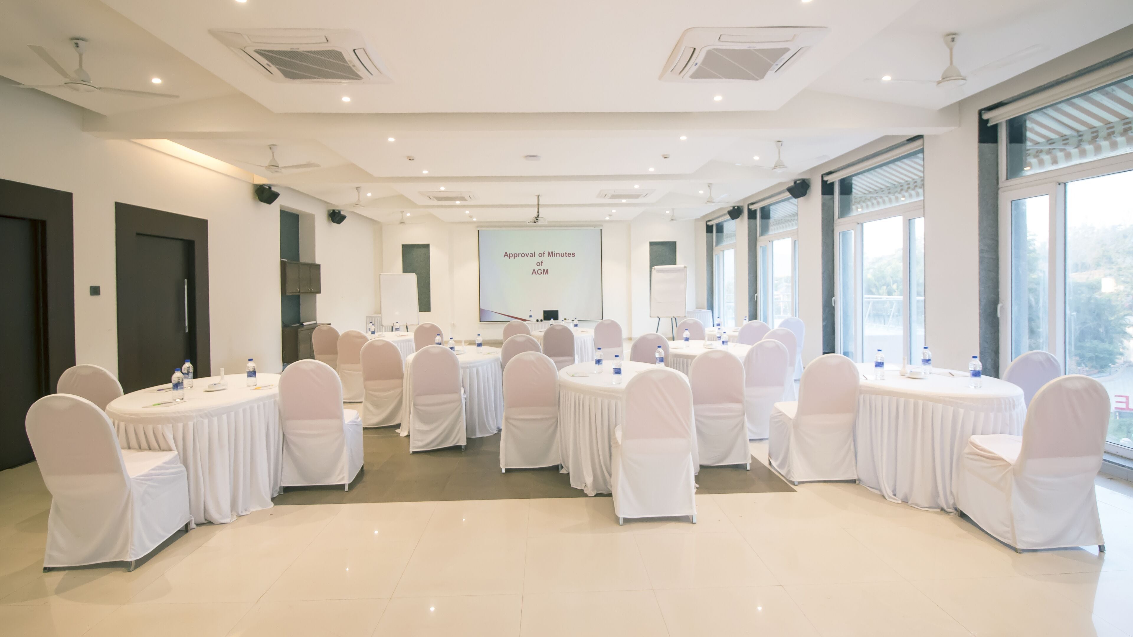 A conference room with round tables and chairs, a projector screen, and large windows.