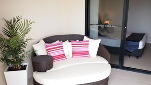 A wicker sofa with white cushions and striped pillows, positioned next to a potted plant. - Edge Apartments Cairns (Cairns North)
