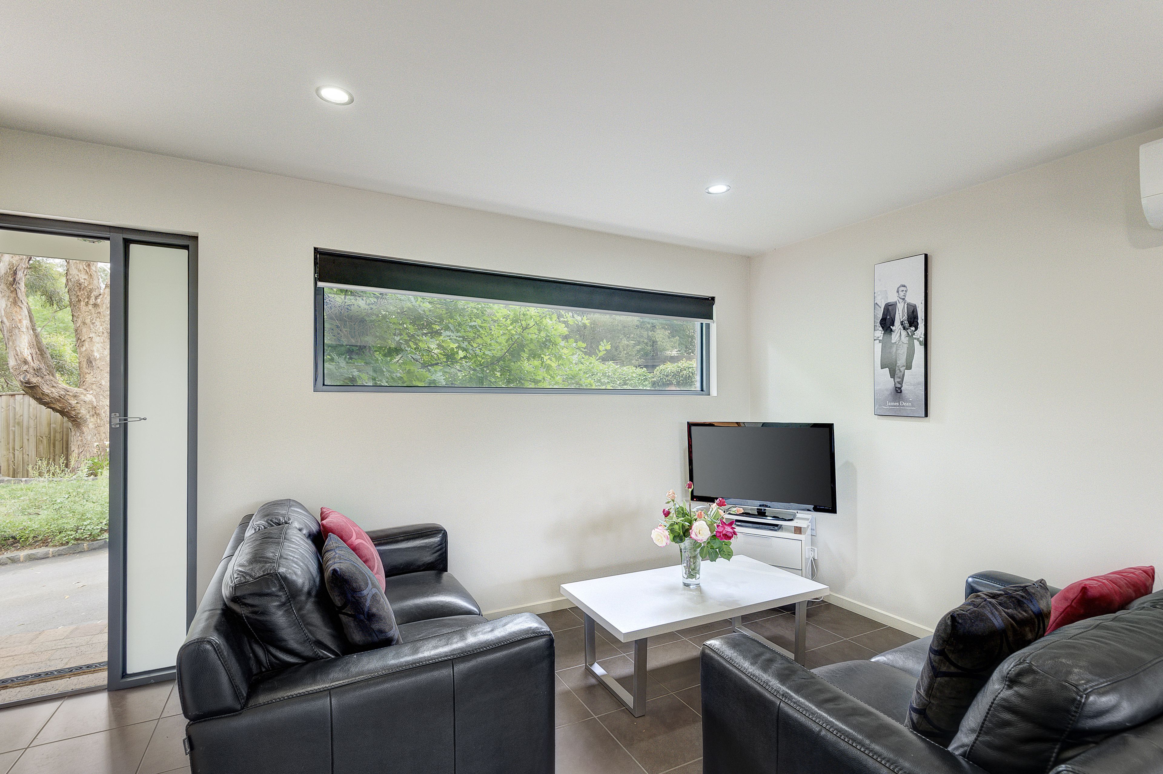 Una sala de estar moderna con sofás de cuero, un televisor de pantalla plana, una mesa de centro y un ventanal con vistas a zonas verdes.
