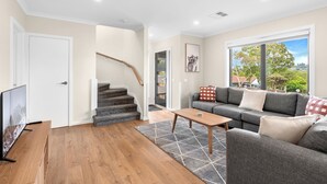 A modern living room with a grey sofa, a wooden coffee table, and a staircase leading to a loft. - Bungunyah Apartments (Croydon)