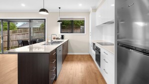 A modern kitchen with a large island, stainless steel appliances, and a view of the backyard. - Bungunyah Apartments (Croydon)