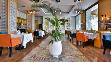 Un restaurante con mesas y sillas, una planta grande en maceta e iluminación decorativa.