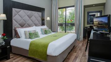 Habitación de hotel con una cama grande, televisión y balcón con cortinas.