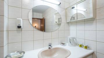 A bathroom with a sink, mirror, soap dispenser, and a coffee maker.