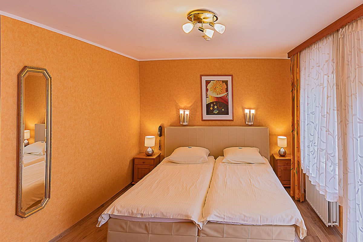 A double bed with a headboard, two bedside tables with lamps, a mirror, and a painting on the wall.