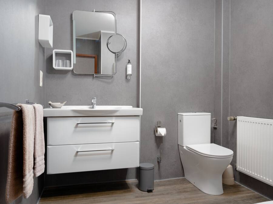 Un baño moderno con tocador blanco, un espejo, un inodoro y un cubo de basura.