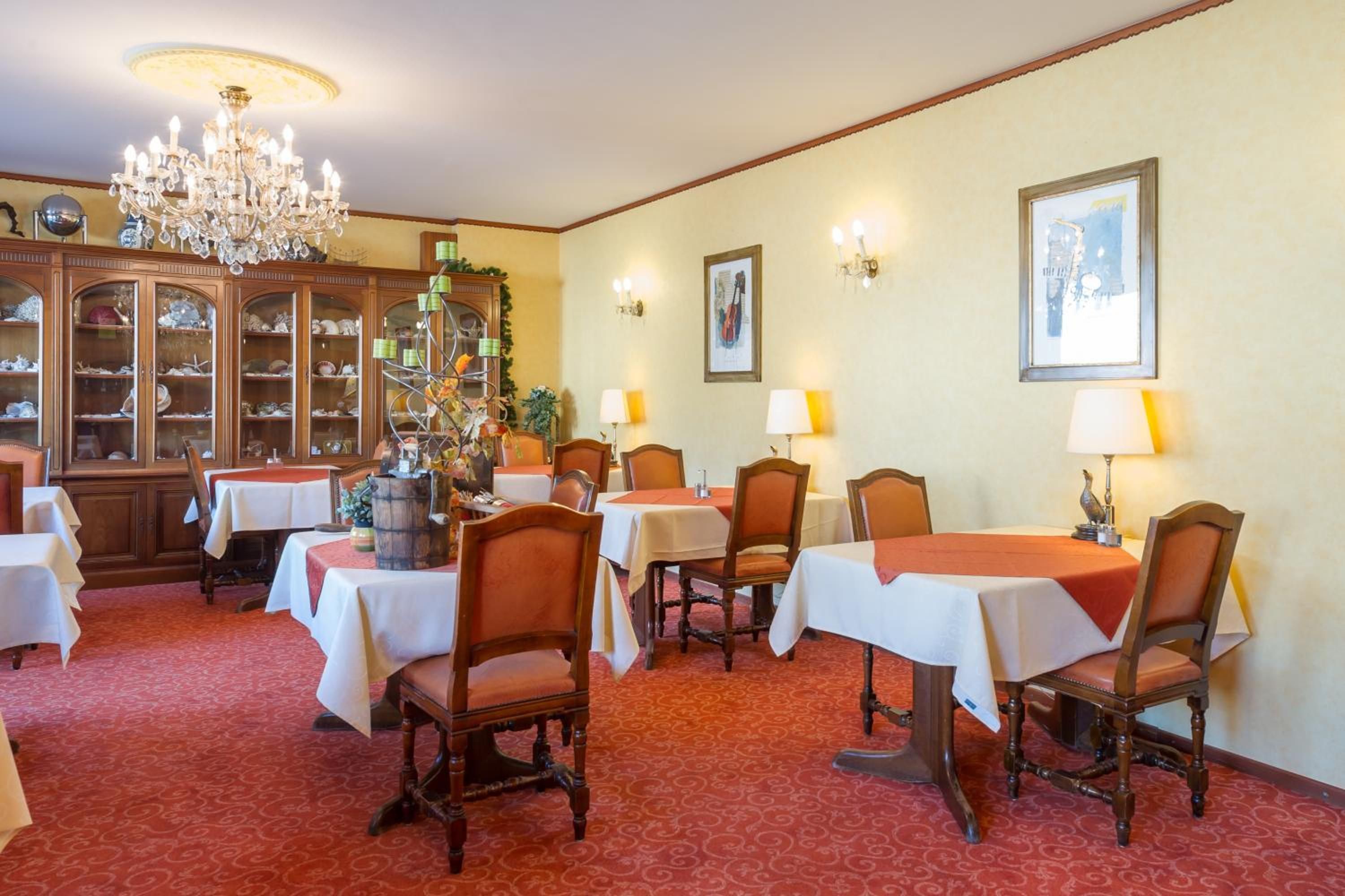 A dining area with tables and chairs, a chandelier, wall-mounted lamps, and a cabinet with glass doors.