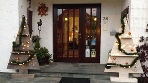 A building entrance with a wooden door, numbered 28, and two Christmas trees decorated with lights and ornaments. - Hostellerie Val Fleuri (Mersch)