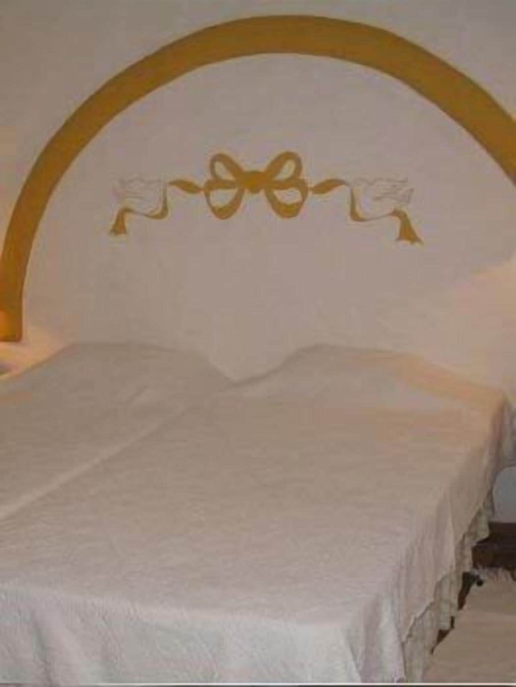 A bed with a white mattress and a headboard with a golden arch and a decorative bow.