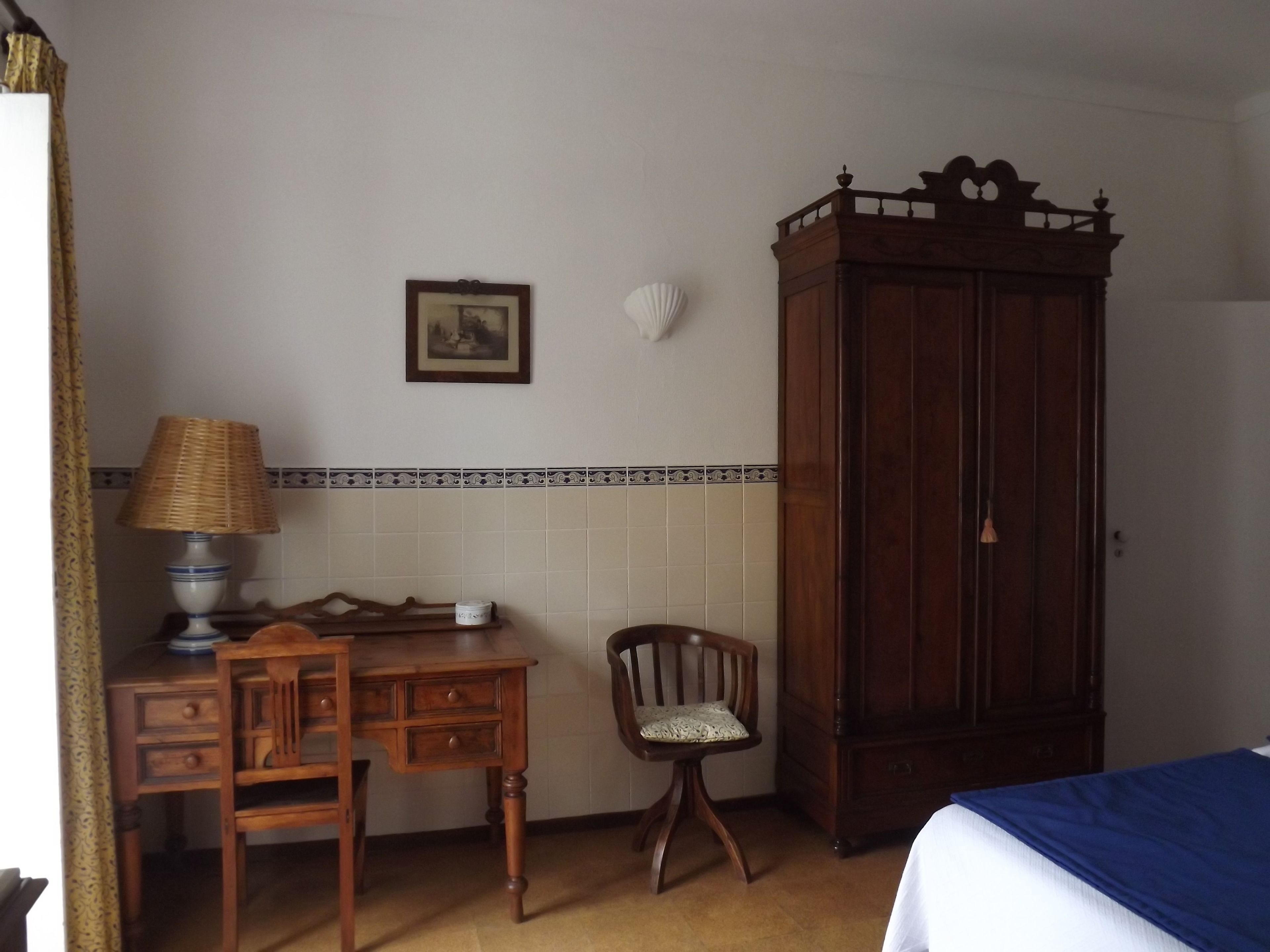 A bedroom with a wooden desk, chair, wardrobe, and a bed with a blue bedspread.