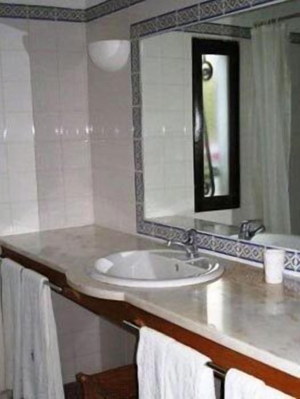 Un baño con lavamanos blanco, un espejo y un perchero para toallas.