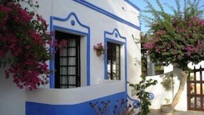 Um edifício branco com detalhes azuis e janelas, rodeado por plantas floridas.