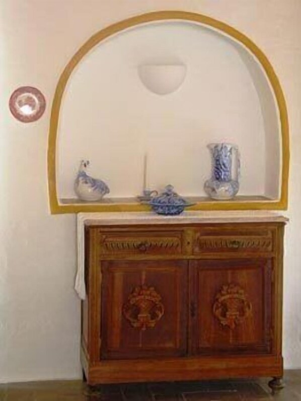 Un mueble de madera con un estante decorativo en la parte superior, un espejo fijado a la pared y una pequeña decoración mural.