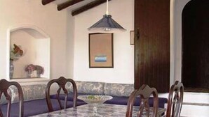 Uma sala de jantar com mesa de mármore, cadeiras de madeira, luminária pendente e um banco de pedra.