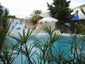 Una piscina rodeada de palmeras y un edificio blanco con techo azul.