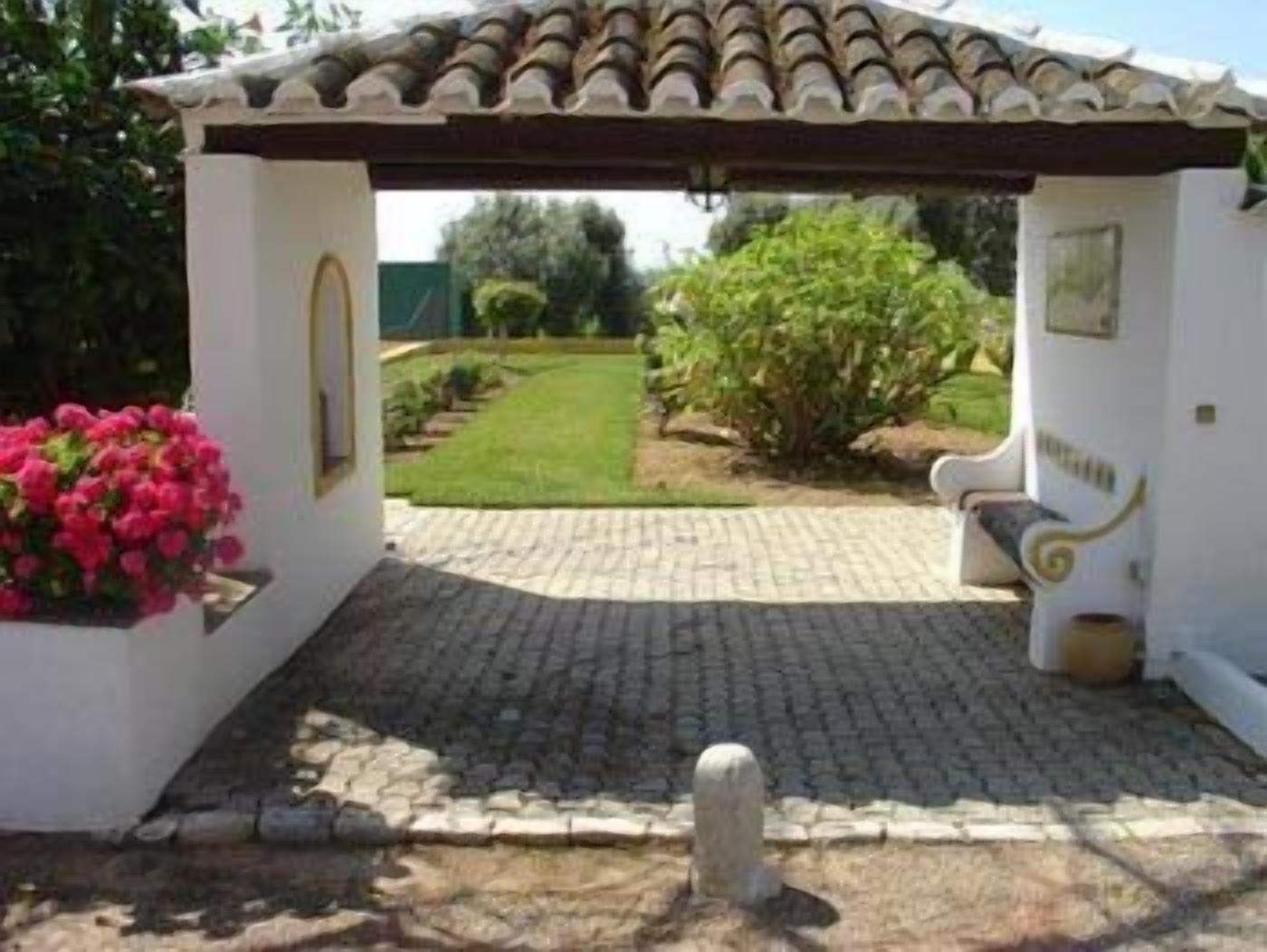 A covered outdoor area with a tiled roof, a bench, and a flower bed.