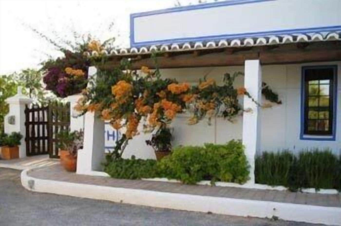 A building with a white facade, a blue door, and a covered porch with hanging flowers.