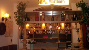 Eine Bar mit einem gut sichtbaren Marlboro-Schild, Regalen voller verschiedener Flaschen und einer dekorativen Pflanze.