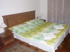 Ein Doppelbett mit floralem Überwurf, zwei Nachttischlampen, ein hölzernes Kopfstück und ein gemustertes Teppich.