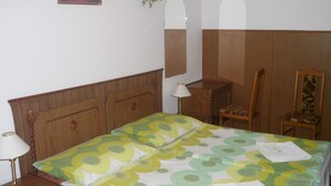 Ein Schlafzimmer mit Bett, Nachttisch, Stuhl, Schreibtisch, Spiegel und einer Wandpflanze.