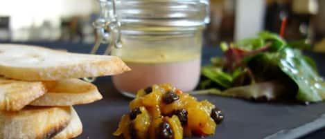 A plate with toasted bread, a small bowl of fruit, and a glass jar of dressing.