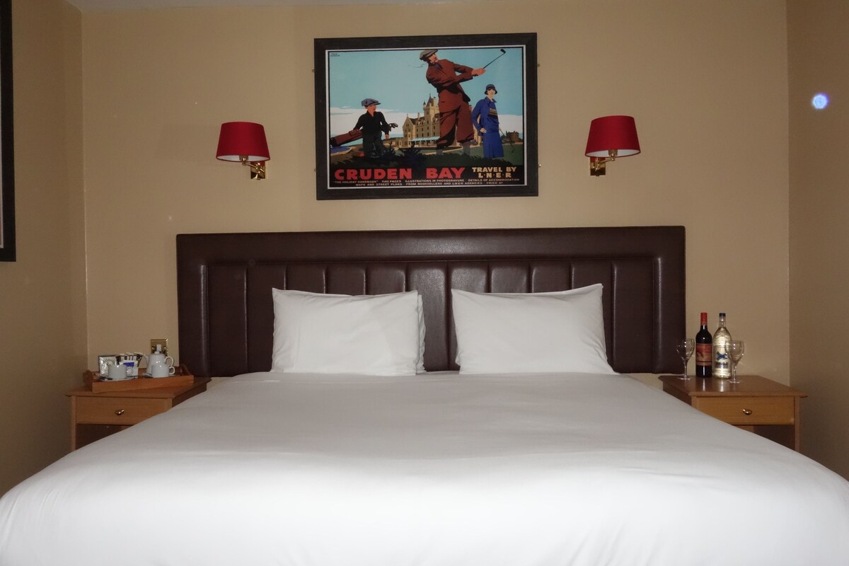 A hotel room with a large bed, two bedside tables, and a poster on the wall.