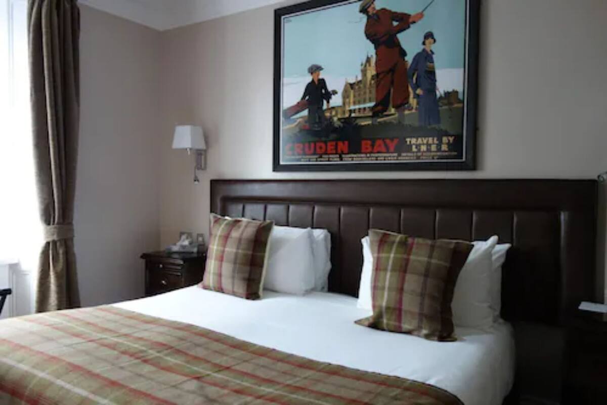 A hotel room with a large bed, two pillows, a nightstand, a lamp, and a poster on the wall.