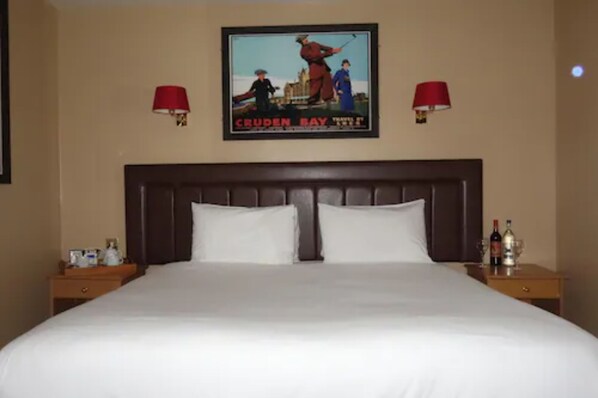 A hotel room with a large bed, two nightstands, a poster on the wall, and two red lamps.