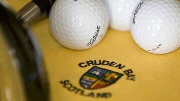 Pelotas de golf y un palo de golf sobre una superficie amarilla con un logo que dice 'CRUDEN BAY SCOTLAND'.