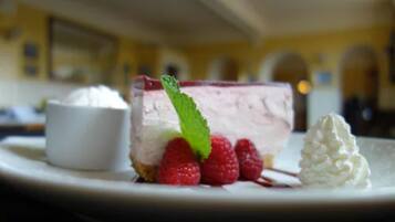 Un postre con una porción de pastel de queso, frambuesas y crema batida sobre un plato.