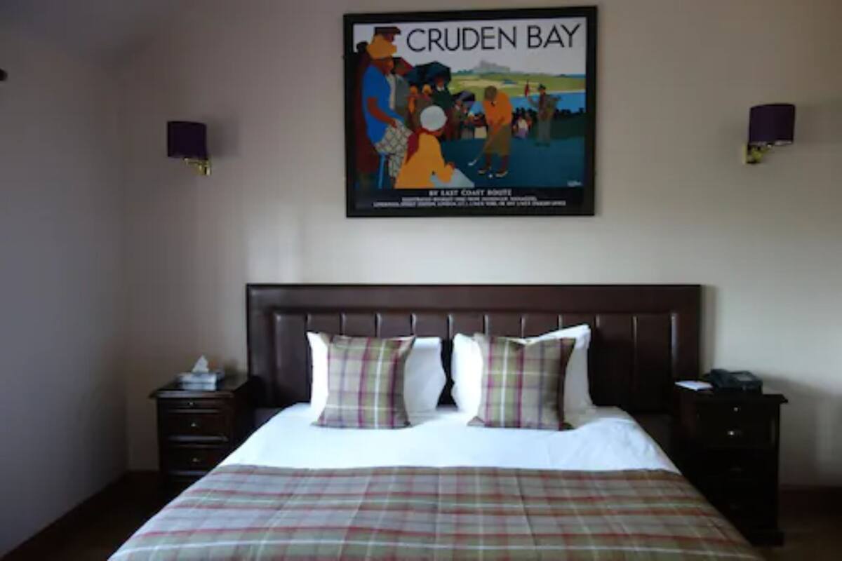 A hotel room with a bed, a nightstand, a wall-mounted lamp, and a poster of a beach scene.