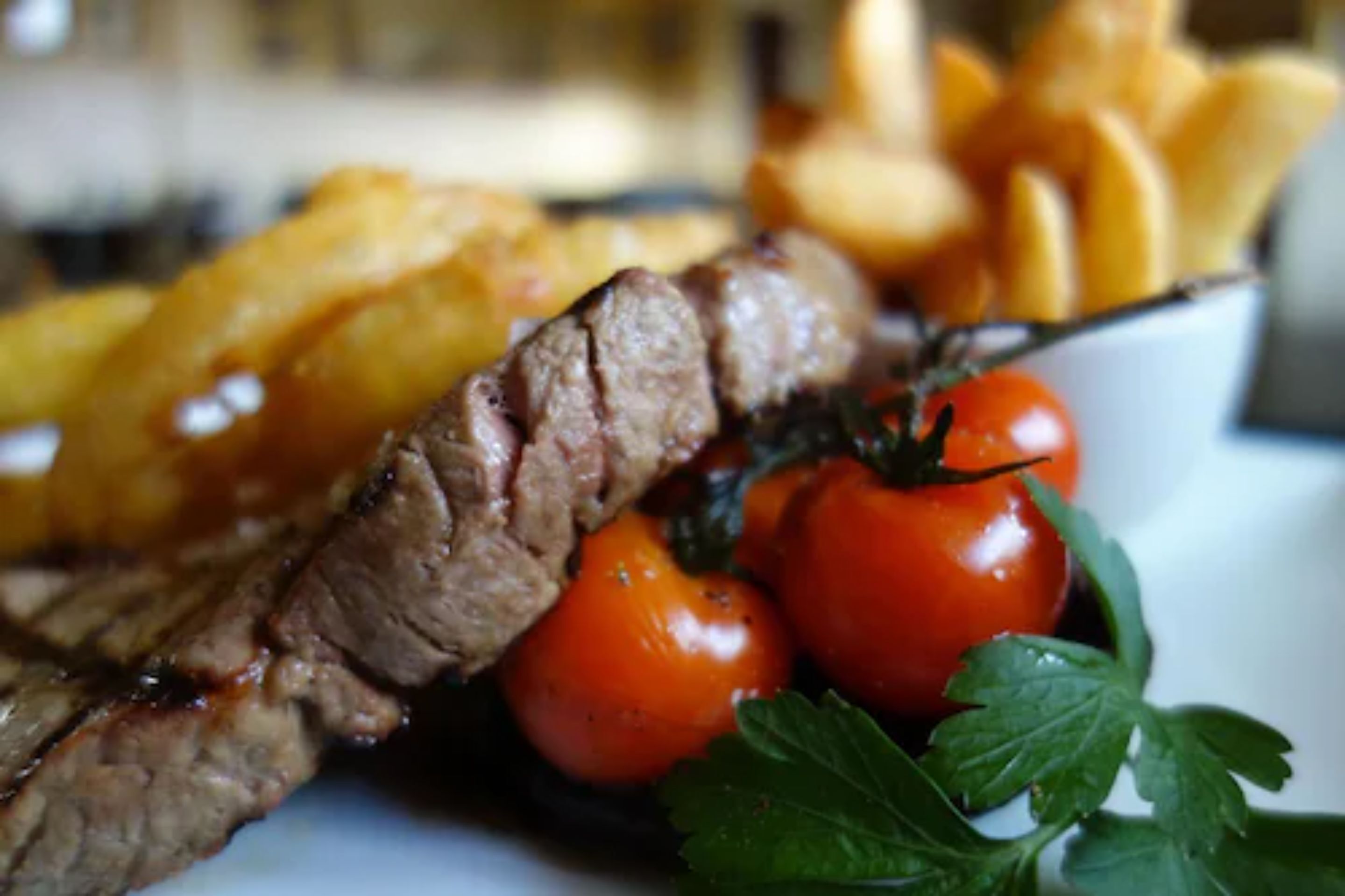 Un plato con bistec en rodajas, tomates cherry y papas fritas.