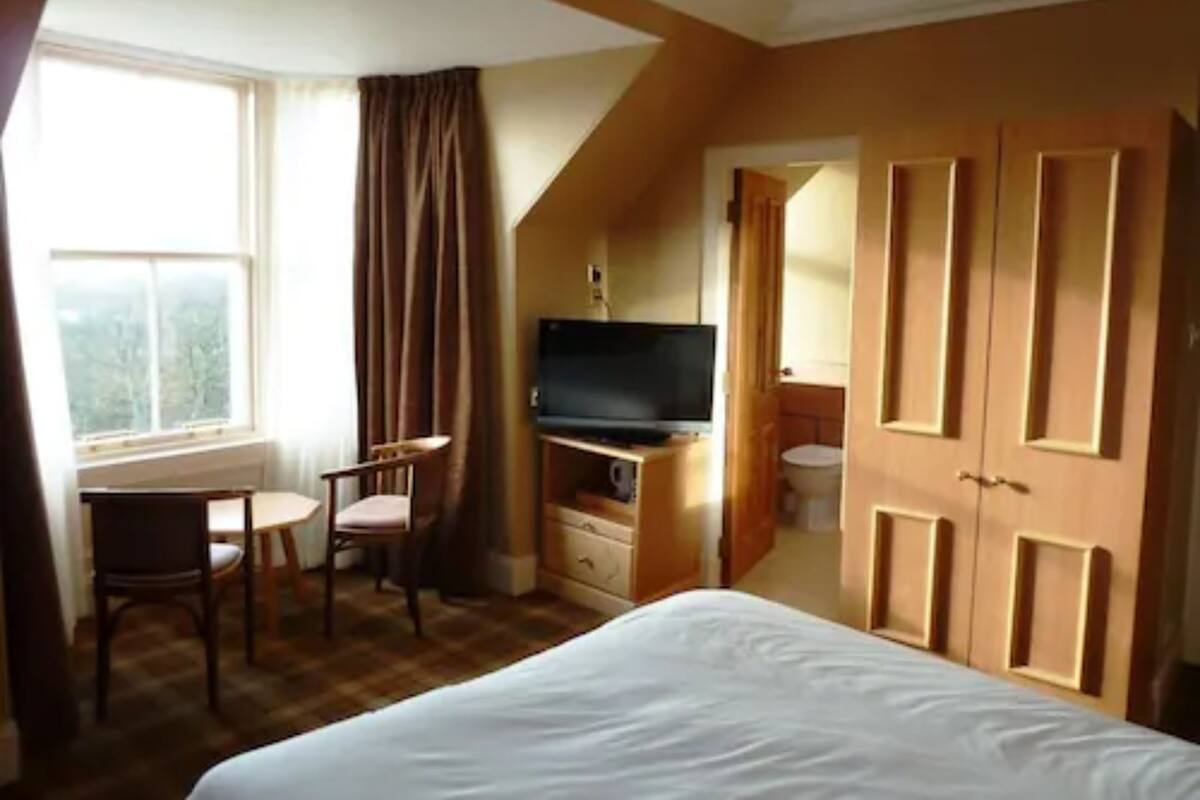 A hotel room with a bed, a desk with a chair, a television, and a wardrobe.