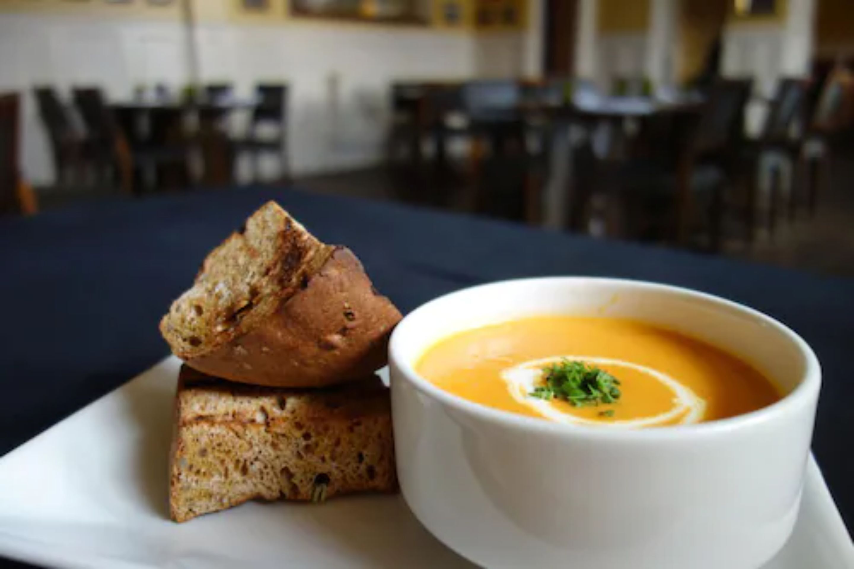 A bowl of soup with a garnish on a white plate, accompanied by a piece of bread.