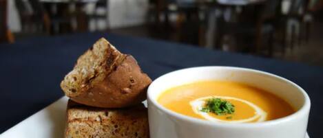 A bowl of soup with a garnish on a white plate, accompanied by a piece of bread.