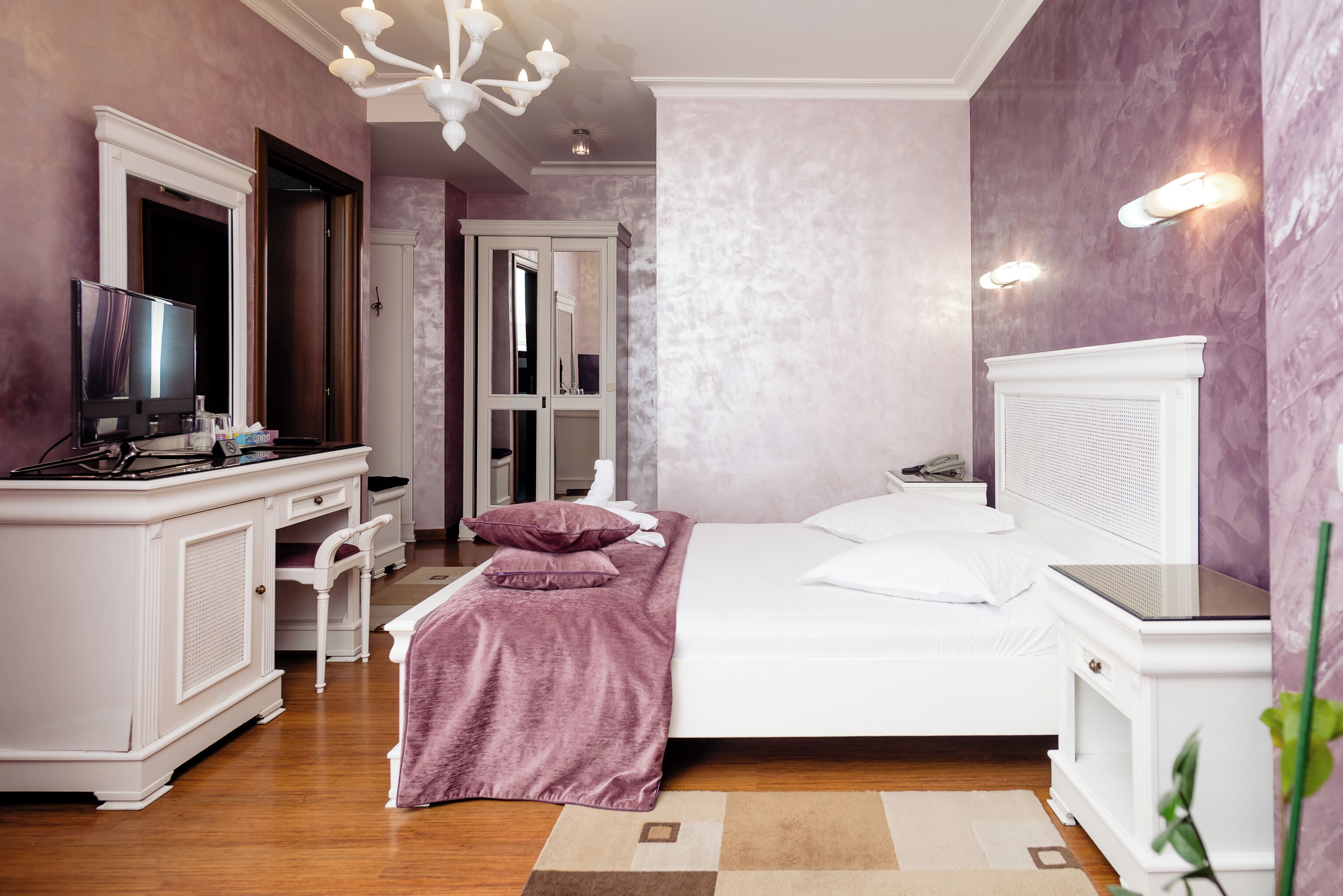 A bedroom with a bed, a desk with a TV, a chair, and a mirror.