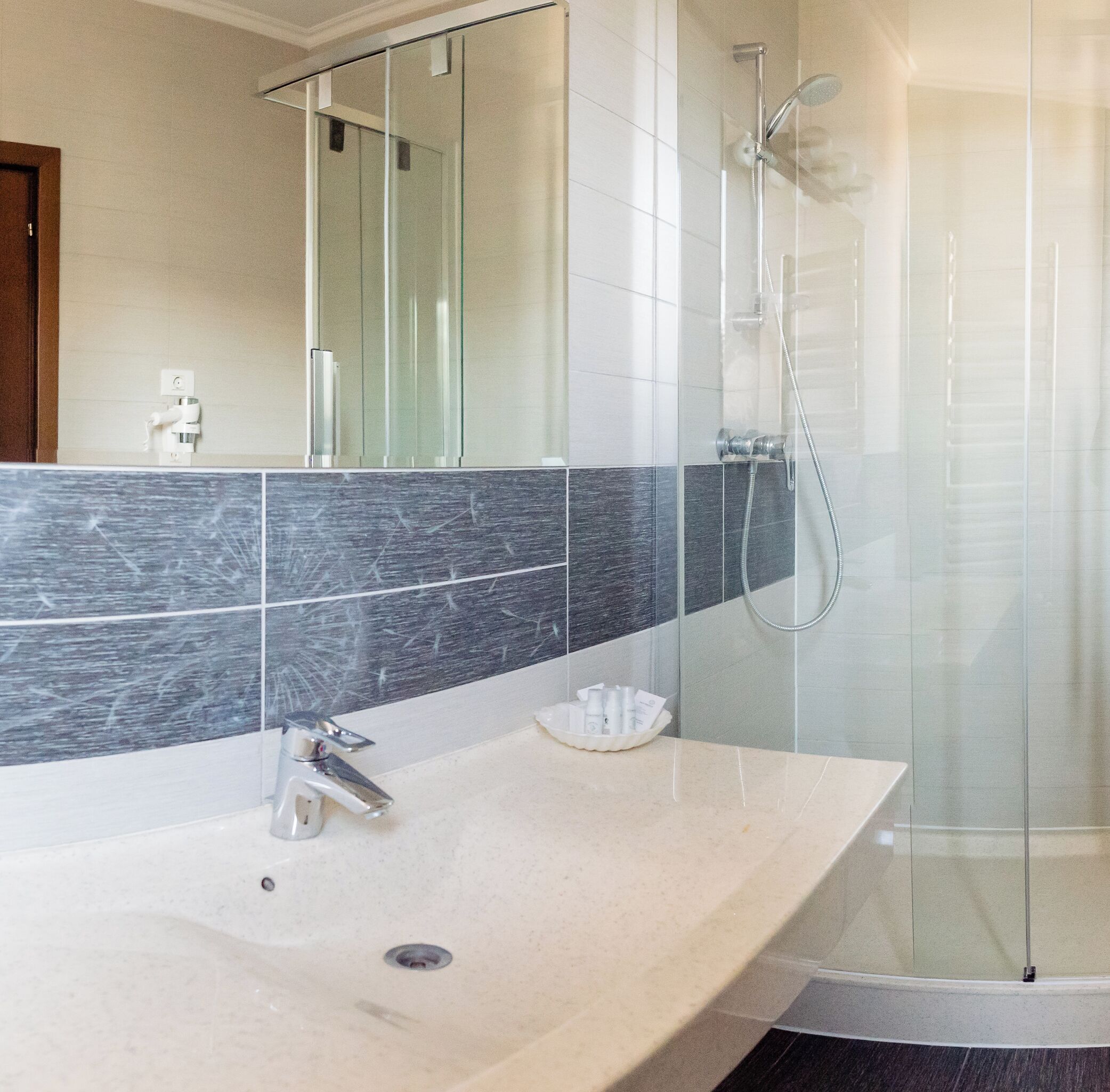 Een moderne badkamer met een grote spiegel, een douchecabine en een wastafel met toiletartikelen.